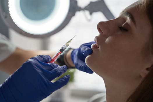 Lip augmentation and correction procedure in a cosmetology salon. The specialist makes an injection in the patient's lips. Beautiful Young Woman's Mouth Receiving Hyaluronic Acid Injection.