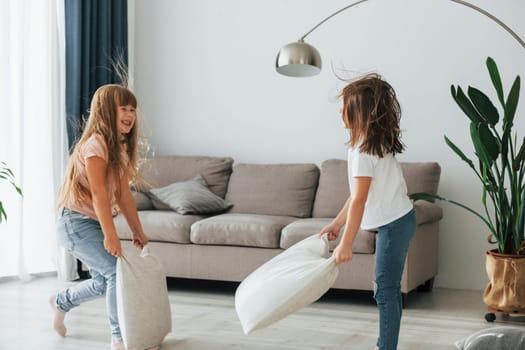 Pillow fight. Kids having fun in the domestic room at daytime together.