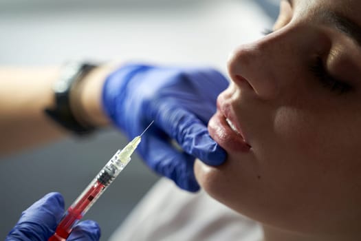 Lip augmentation and correction procedure in a cosmetology salon. The specialist makes an injection in the patient's lips. Beautiful Young Woman's Mouth Receiving Hyaluronic Acid Injection.