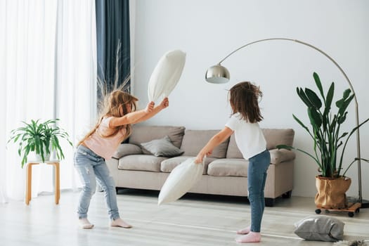 Pillow fight. Kids having fun in the domestic room at daytime together.