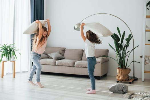 Pillow fight. Kids having fun in the domestic room at daytime together.