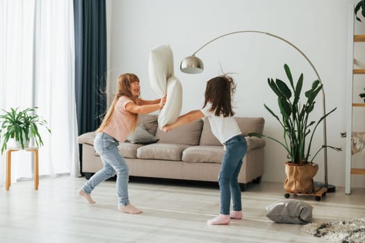 Pillow fight. Kids having fun in the domestic room at daytime together.