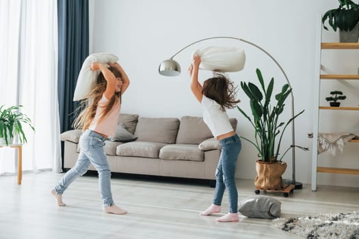 Girls are playing pillow fight game. Kids having fun in the domestic room at daytime together.