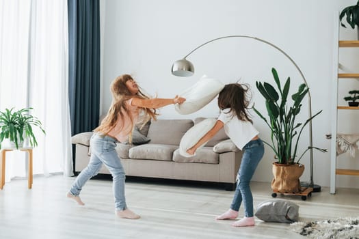 Girls are playing pillow fight game. Kids having fun in the domestic room at daytime together.