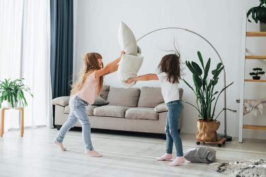 Girls are playing pillow fight game. Kids having fun in the domestic room at daytime together.