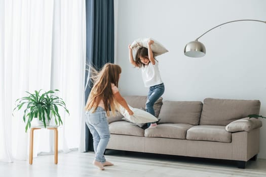 Running with pillows. Kids having fun in the domestic room at daytime together.