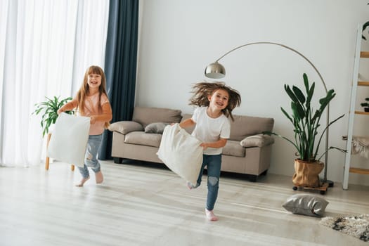 Running with pillows. Kids having fun in the domestic room at daytime together.