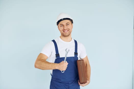 Holding brown case. Worker in uniform and hard hat standing in the studio with equipment.