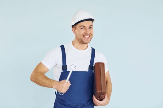 Holding brown case. Worker in uniform and hard hat standing in the studio with equipment.