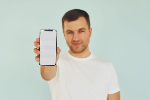 Man in casual clothes standing in the studio with phone in hands.