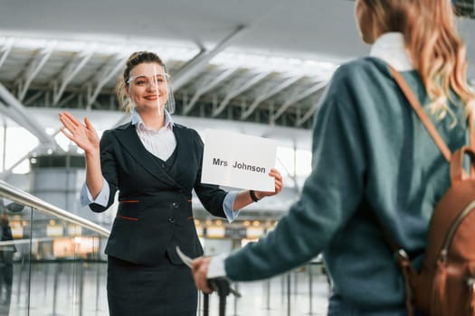 Woman with plate with text. Young female tourist is in the airport at daytime.