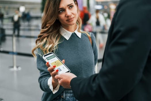 Certificate of vaccination in the phone. Young female tourist is in the airport at daytime.