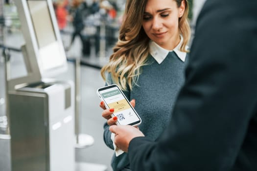 Certificate of vaccination in the phone. Young female tourist is in the airport at daytime.