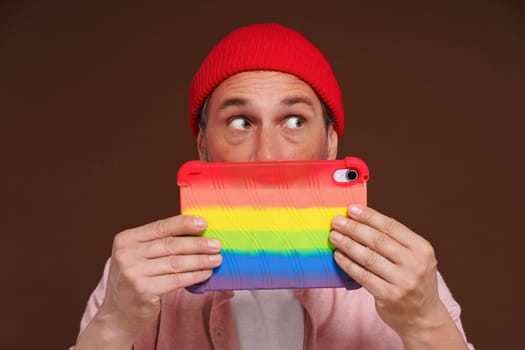 Gay man depicted feeling ashamed sexual orientation online, looking out with fear over tablet LGBT coloring. man in digital world represents negative emotions associated with secrecy and hidden personal identity. High quality photo