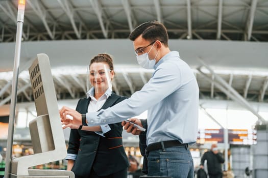 Employee helping using terminal. Young businessman in formal clothes is in the airport at daytime.