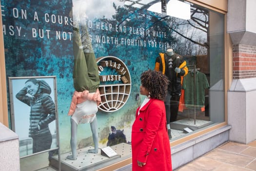 an African American woman looks at a shop window at a poster calling for not littering the earth with plastic waste, Maasmechelen, Belgium,February 17,2023. High quality photo