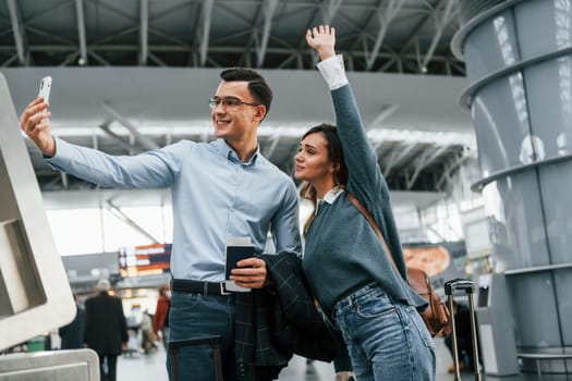 Using phone to make selfie. Young couple is in the airport together.