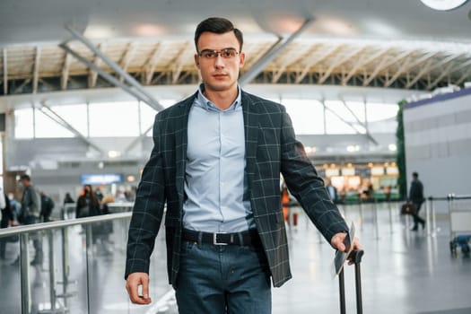 With lugagge. Young businessman in formal clothes is in the airport at daytime.