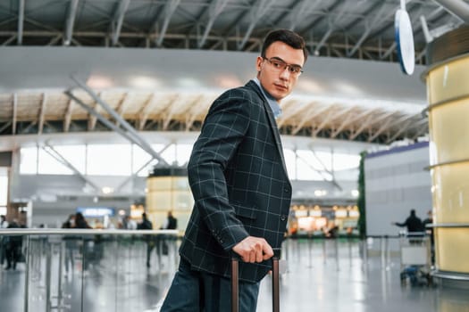 With lugagge. Young businessman in formal clothes is in the airport at daytime.