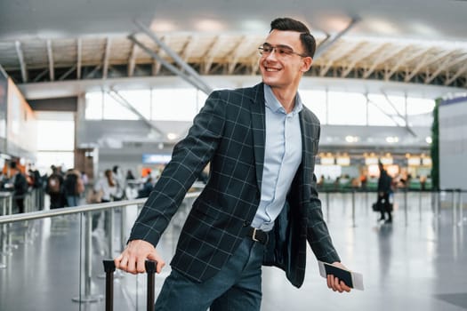 With lugagge. Young businessman in formal clothes is in the airport at daytime.