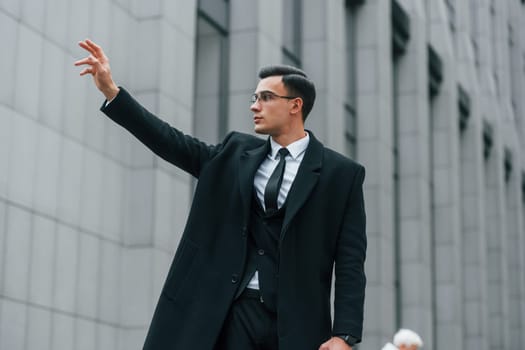 Calling taxi. Businessman in black suit and tie is outdoors in the city.