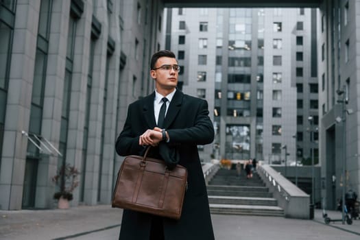 Front view. Businessman in black suit and tie is outdoors in the city.