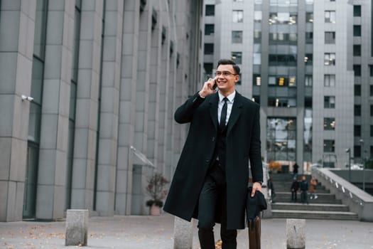 In formal clothes. Businessman in black suit and tie is outdoors in the city.