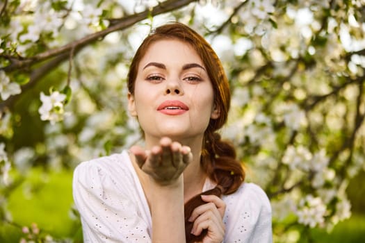 openly smiling woman against the backdrop of a flowering tree stretches her palms to the camera. High quality photo