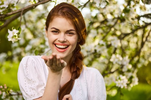 openly smiling woman against the backdrop of a flowering tree stretches her palms to the camera. High quality photo