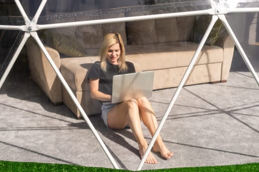 Transparent bubble tent at glamping, Lush forest around and interior. Woman with laptop.