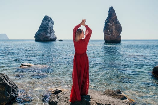 Woman travel sea. Young Happy woman in a long red dress posing on a beach near the sea on background of volcanic rocks, like in Iceland, sharing travel adventure journey