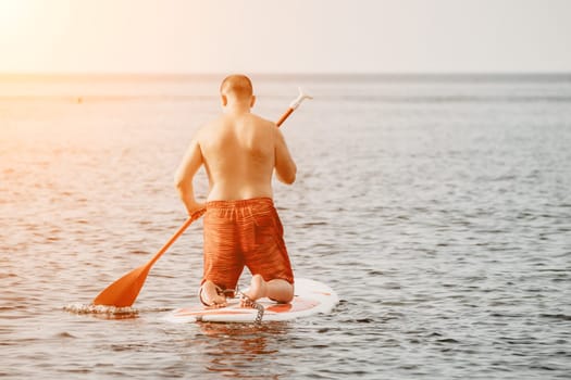 Active mature male paddler with his paddleboard and paddle on a sea at summer. Happy senior man stands with a SUP board. Stand up paddle boarding - outdor active recreation in nature