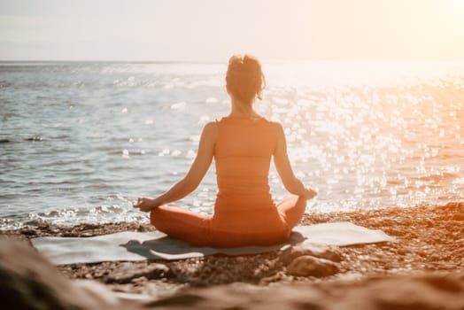 The woman in a red suit practicing yoga on stone at sunrise near the sea. Young beautiful girl in a red bathing suit sits on the seashore in lotus position. Yoga. Healthy lifestyle. Meditation