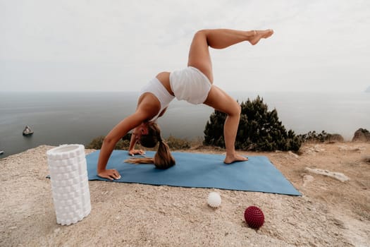 Middle aged well looking woman with black hair doing Pilates with the ring on the yoga mat near the sea on the pebble beach. Female fitness yoga concept. Healthy lifestyle, harmony and meditation.