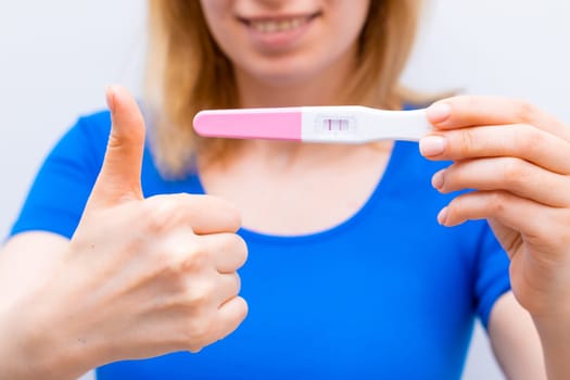 Smiling woman shows sign like and holding a positive pregnancy test.