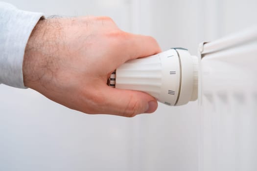 Man hand regulates temperature knob of the heating radiator to reduce heating costs.