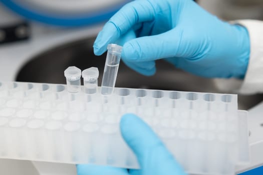 Female scientist in protective gloves picks up samples from the centrifuge and puts into the rack. Medicine and research concept.