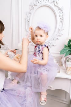 Baby girl elegant dress. A one-year-old girl in a puffy dress and a cute bow poses against the backdrop of a bright room with a dressing table and flowers