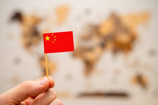 China flag in mans hand on the wooden world map background. Global economy and geopolitics concept.