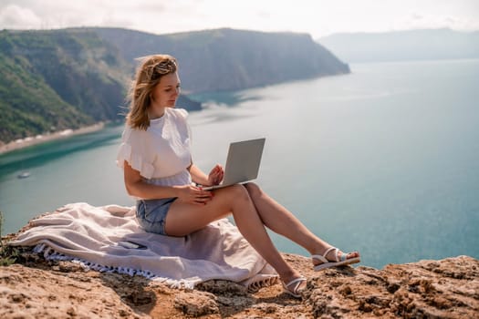 Freelance women sea working on the computer. Good looking middle aged woman typing on a laptop keyboard outdoors with a beautiful sea view. The concept of remote work