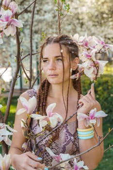 Magnolia flowers. Happy woman enjoys by blooming magnolia tree and sniffs it flowers with closed eyes in spring garden. Portrait