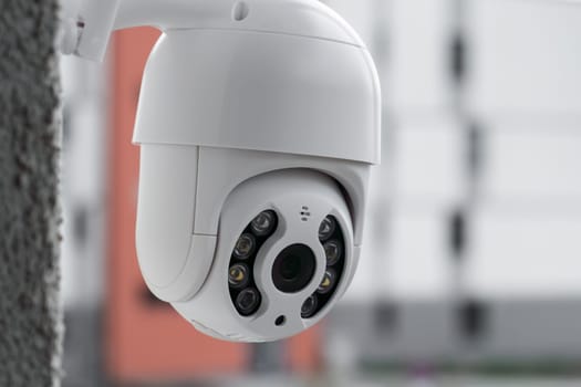Modern CCTV camera on a wall with a blurred multi-storey building on the background. Surveillance and monitoring of outdoor to protect against thieves