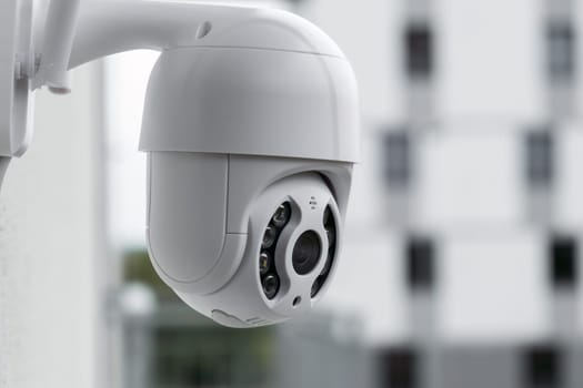 Modern CCTV camera on a wall with a blurred multi-storey building on the background. Surveillance and monitoring of outdoor to protect against thieves