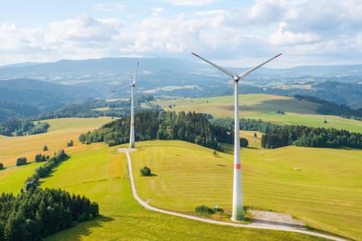 Panoramic view of windmills in the wind farm in the yellow field and mountains on the background. Production of green and renewable energy.