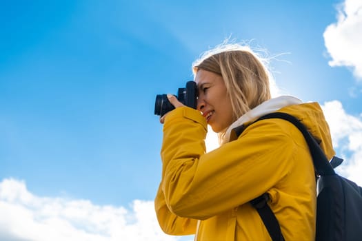 Beautiful travel woman with backpack takes photos by the camera against blue sky with clouds.