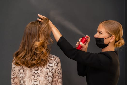 Women salon hairstyle. Hairdresser uses hairspray on client's hair in salon, Portrait of two beautiful women.