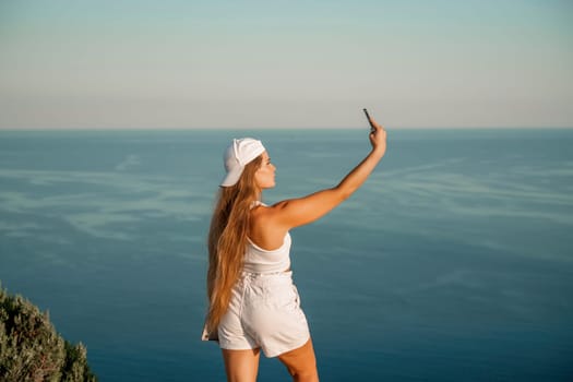 Selfie woman in a cap, white tank top and shorts makes a selfie shot mobile phone post photo social network outdoors on the background of the sea beach people vacation lifestyle travel concept