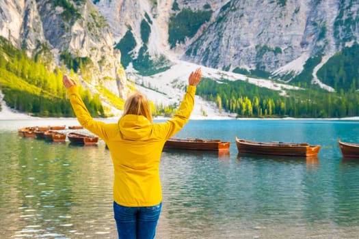 Tourist raised her hands and enjoys the view of Lake Braies with wooden boats in the Dolomites Alps. Trip to Italy in autumn