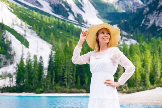 Smiling young woman on the Lake Braies in a white fluttering dress and hat on a sunny day