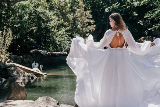 a beautiful woman in a long white dress looks into the distance at a beautiful lake with swans